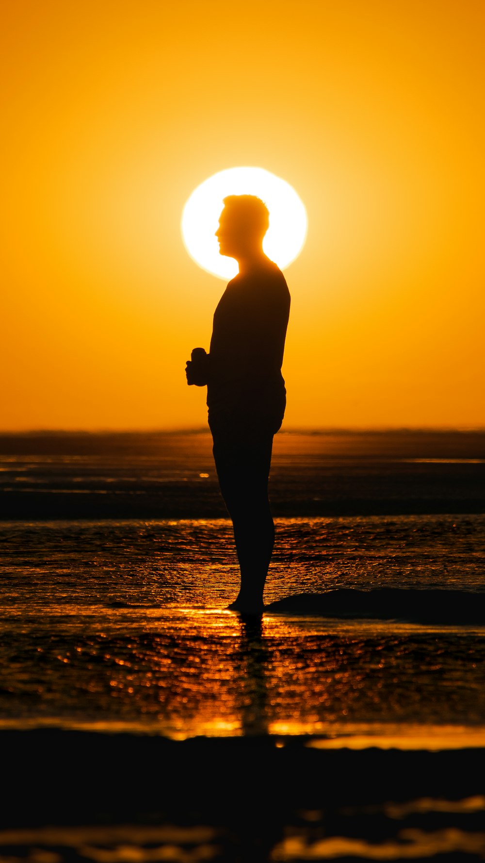 silhueta do homem em pé na praia durante o pôr do sol