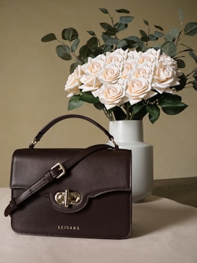 A stylish luxury handbag resting on a marble table beside a fresh bouquet of flowers.
