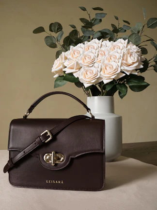 A chic beige tote bag resting on a marble table beside a fresh bouquet of flowers.