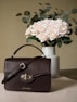 brown leather handbag beside white flower vase