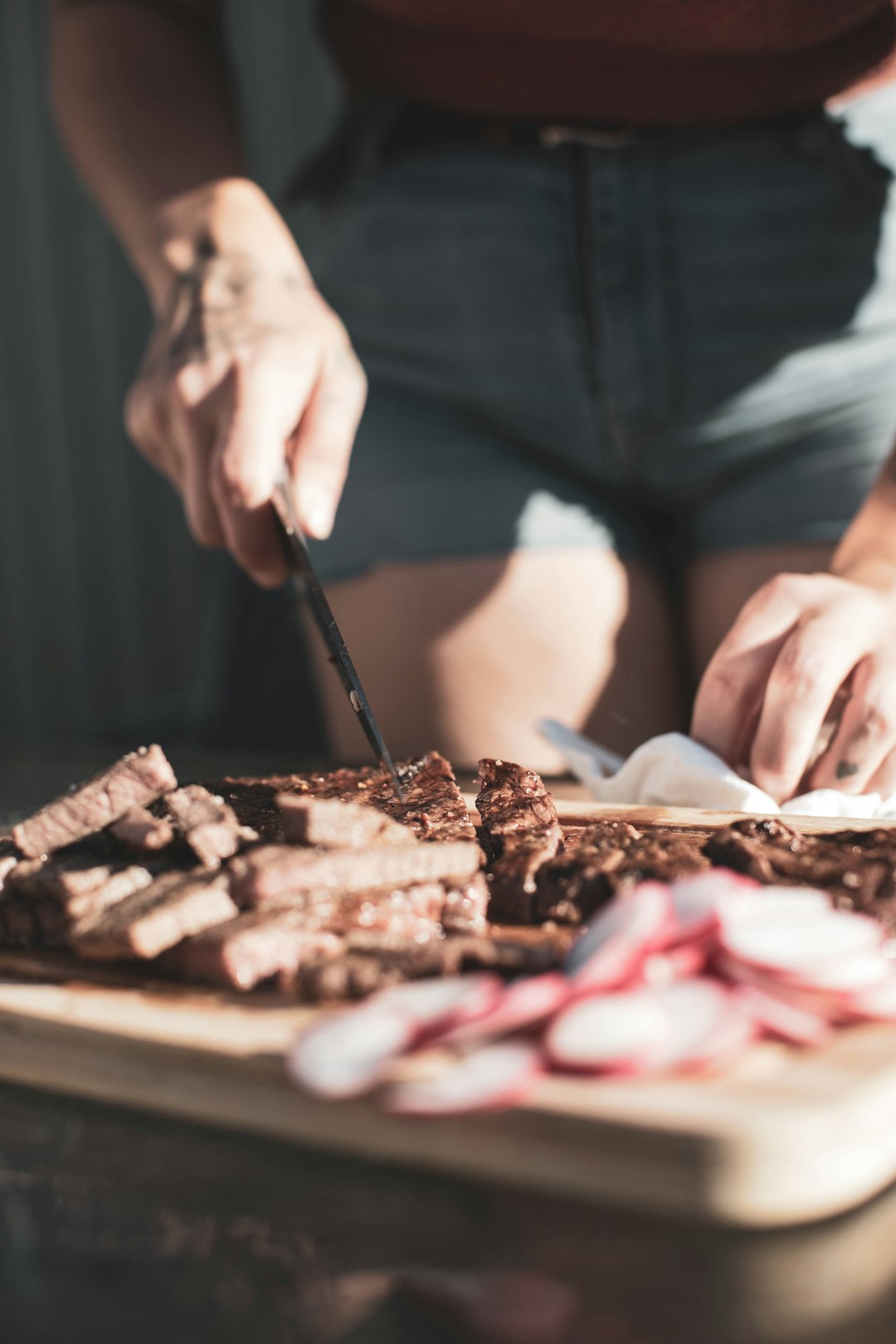 person slicing meat on brown wooden chopping board
