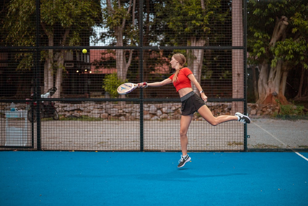 Mujer con camiseta sin mangas roja y pantalones cortos negros sosteniendo raqueta de tenis