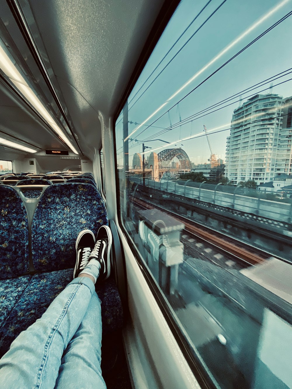 person in blue denim jeans and black sneakers sitting on train seat