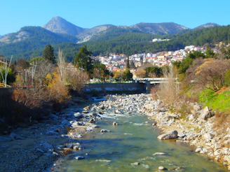 A serene view of the Ceira river flowing gently beside the traditional schist houses of Góis under a clear blue sky.