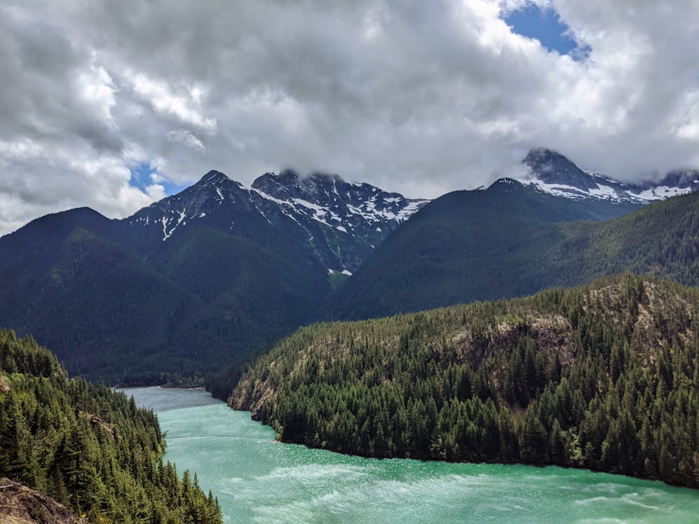 green and brown mountains near body of water under white clouds during daytime