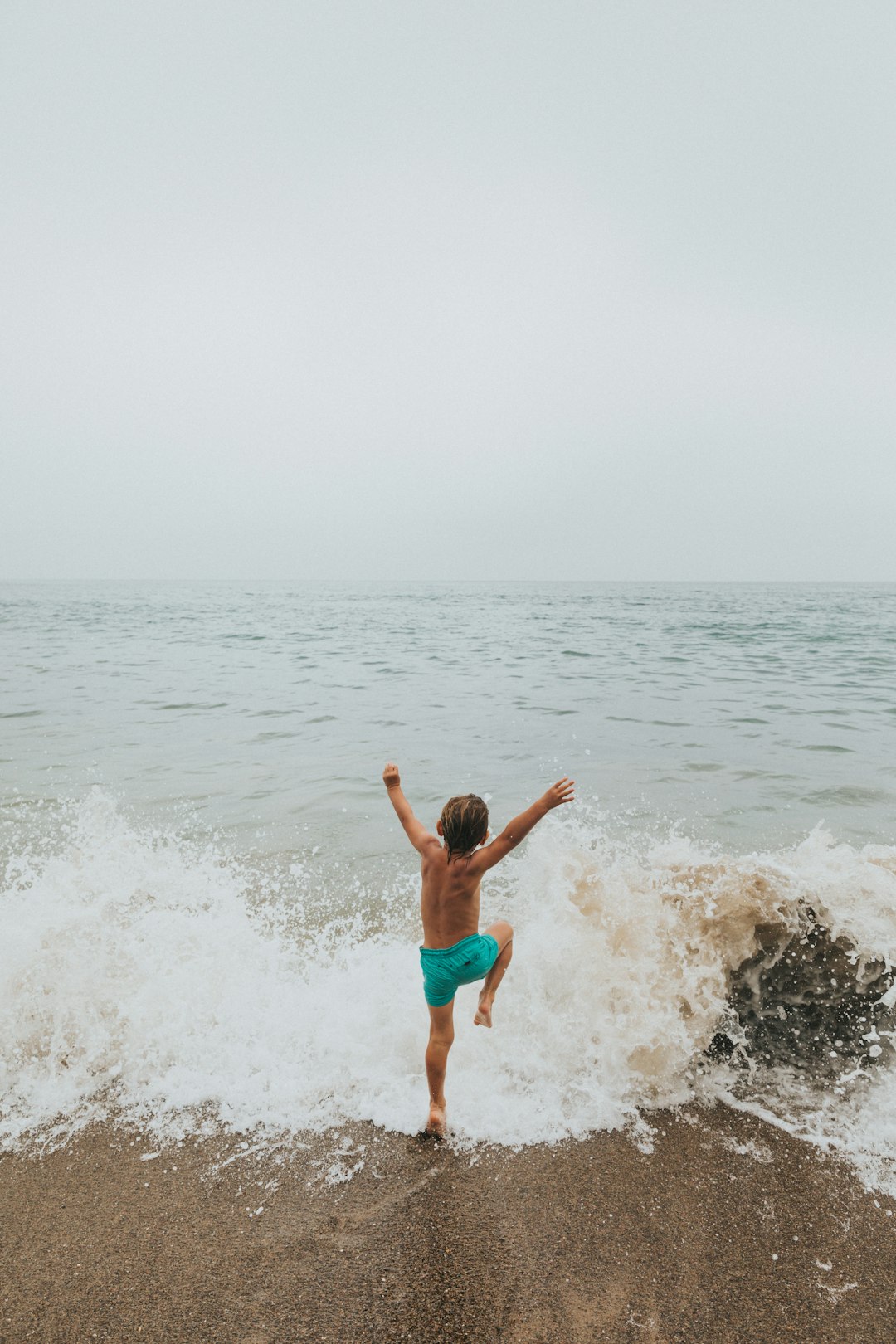 2 boys in blue shorts jumping on beach during daytime