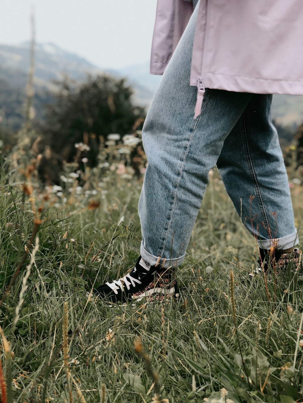 person in blue denim jeans and black and white sneakers standing on green grass field during