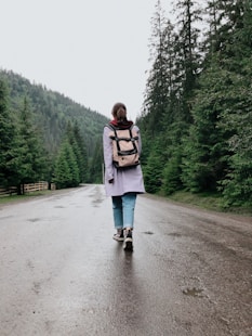 woman in white jacket and blue denim jeans standing on gray asphalt road during daytime