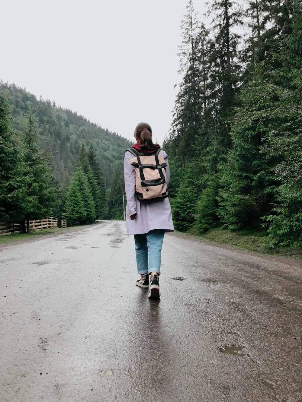 woman in white jacket and blue denim jeans standing on gray asphalt road during daytime