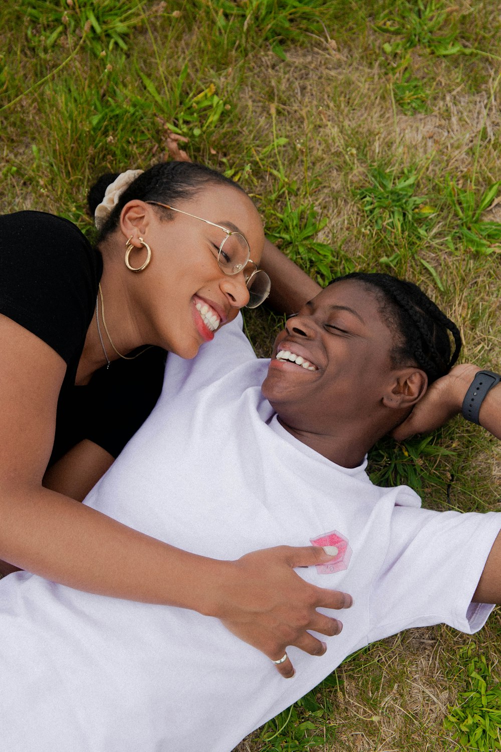 woman in white crew t-shirt beside woman in black tank top lying on green grass