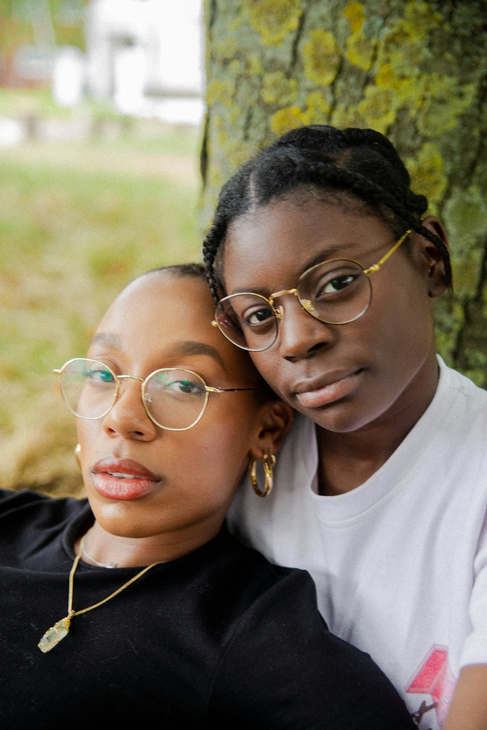 two women wearing gold framed eyeglasses sitting under a tree