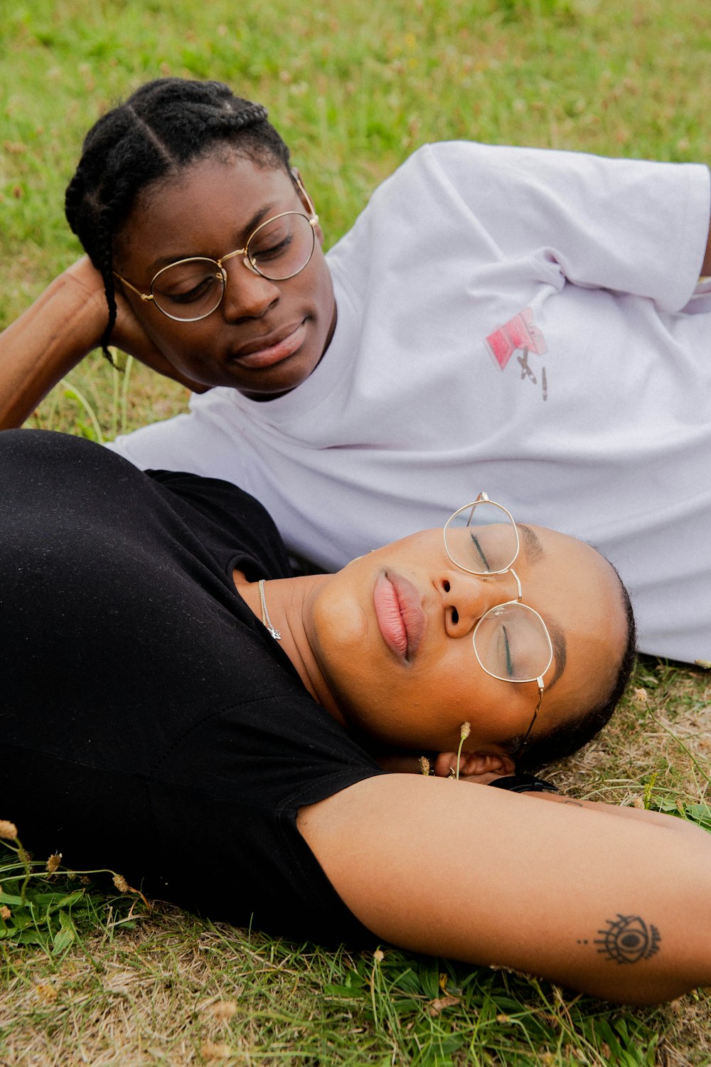 woman in white crew neck shirt wearing silver framed eyeglasses lying on green grass during daytime