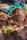 A close-up view of a pile of soil mixed with bits of organic material, such as leaves and twigs. The scene is surrounded by green plants, with hints of purple and brown colors in the background, suggesting an outdoor or garden setting.