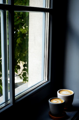 A warm, inviting shot of freshly brewed coffee beside a window overlooking the lush green mountains of the Eje Cafetero region.