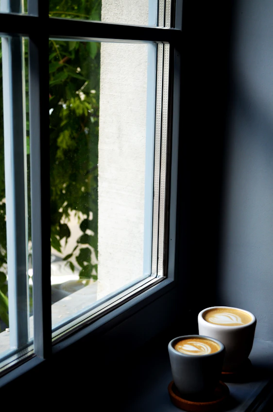 A warm, inviting shot of freshly brewed coffee beside a window overlooking the lush green mountains of the Eje Cafetero region.