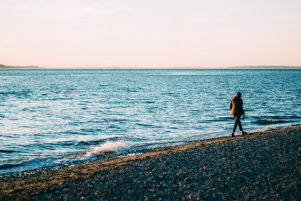 woman in black jacket walking on seashore during daytime