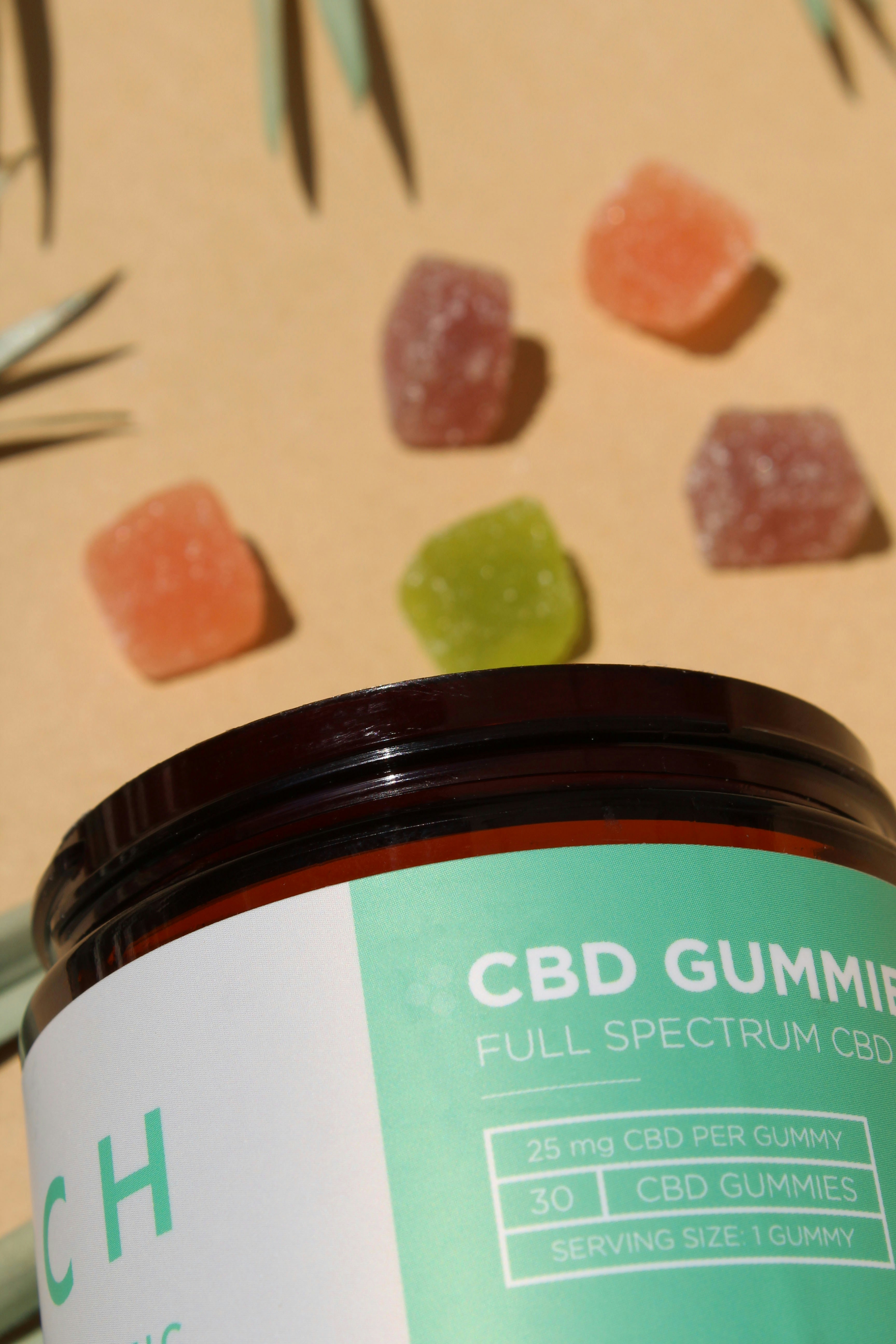Colorful CBD gummies in clear glass jar, bright cheerful product shot on white surface