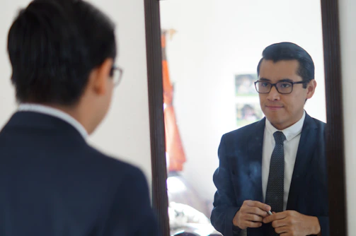 A stylish man adjusting his blazer in front of a mirror, embodying confidence.