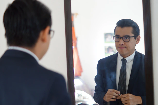 A sophisticated man adjusting his blazer in front of a mirror, showcasing refined fashion.