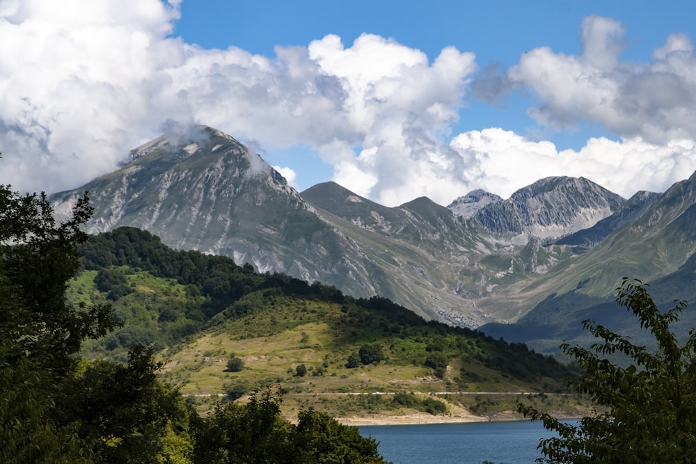 Grüne und weiße Berge in der Nähe von Gewässern unter weißen Wolken und blauem Himmel tagsüber