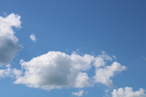 A clear sky filled with fluffy white clouds gently floating against a bright blue backdrop. The clouds vary in size and shape, giving a sense of lightness and calm.