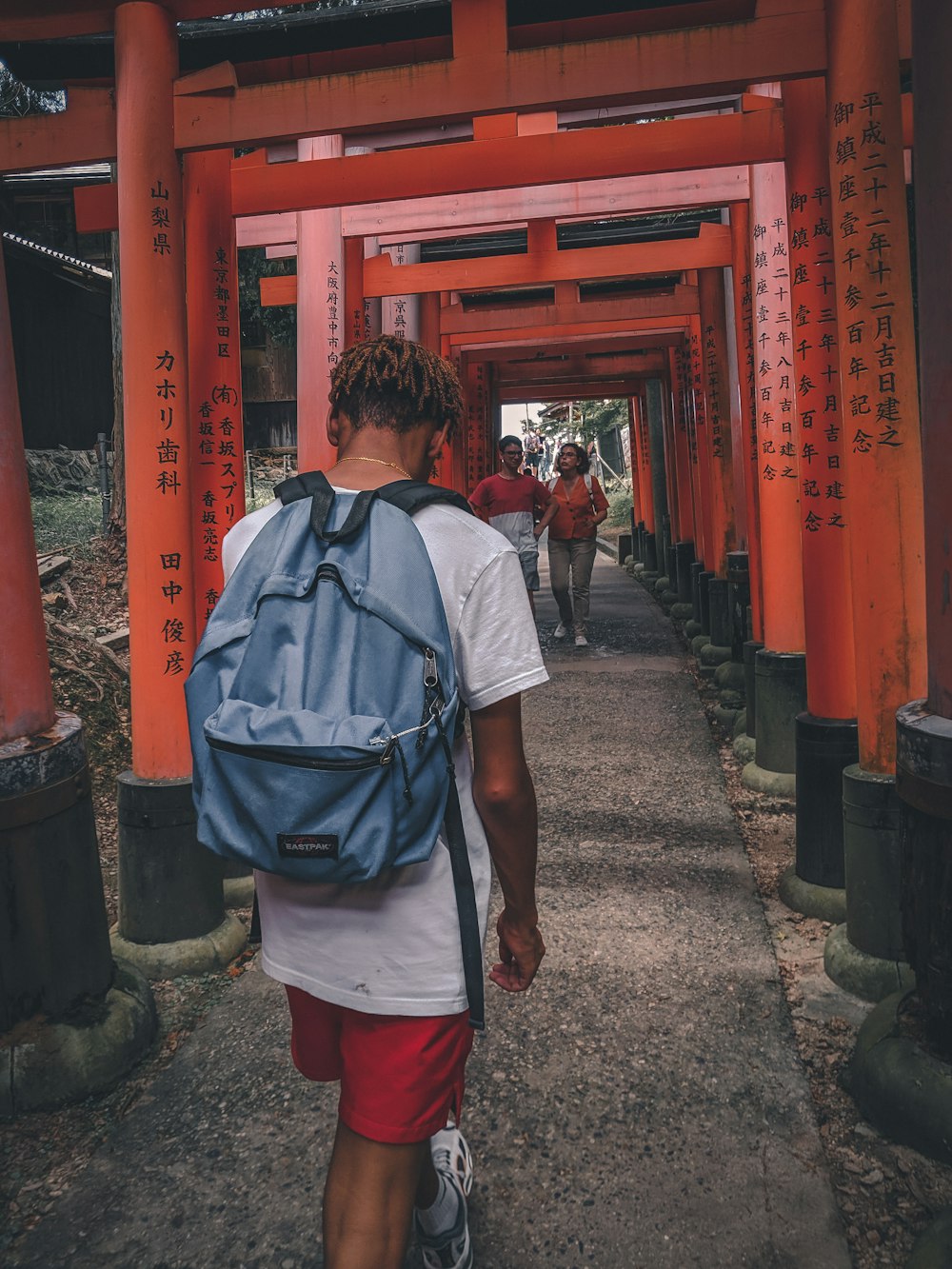 man in white shirt with blue backpack standing near red metal gate during daytime