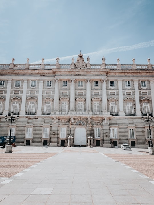 people walking in front of brown concrete building during daytime in Royal Palace of Madrid Spain