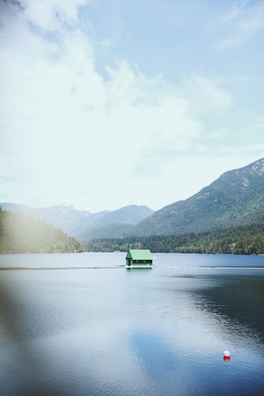 green boat on lake near green mountains during daytime in Capilano River Regional Park Canada