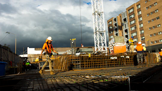 A construction site with workers in orange and navy blue safety gear actively building a modern structure.