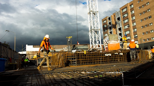 Construction workers collaborating on a building site with orange safety gear.