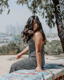 A vibrant outdoor portrait of a young woman smiling naturally while sitting on a sunlit park bench.
