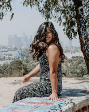 A vibrant outdoor portrait of a young woman smiling naturally while sitting on a sunlit park bench.