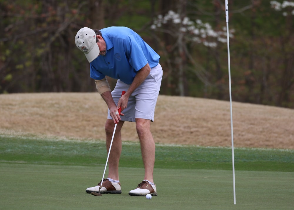 파란색 셔츠와 흰색 반바지를 입은 남자가 낮에 골프를 치고 있다