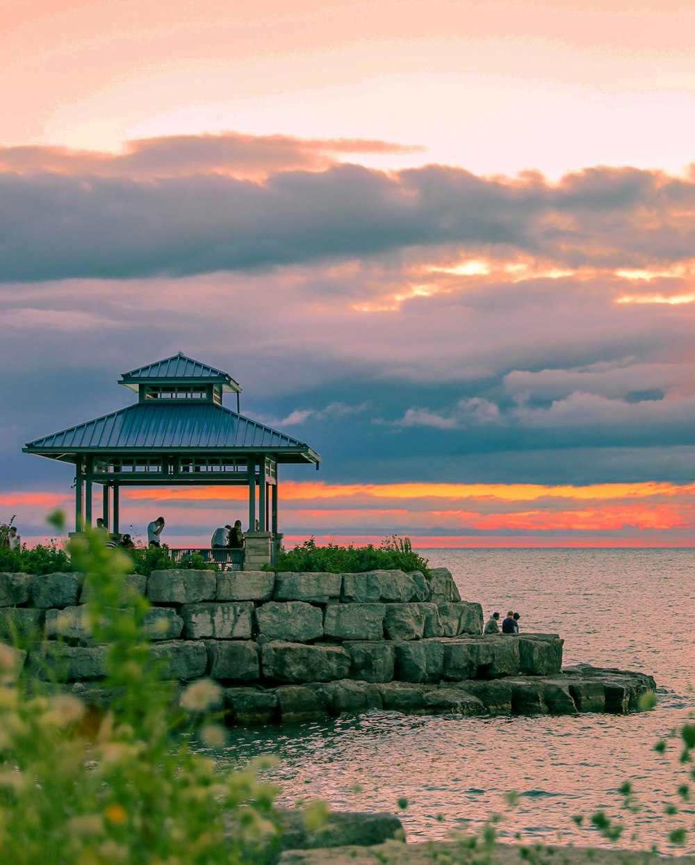 brown wooden gazebo on gray rock formation near body of water during daytime