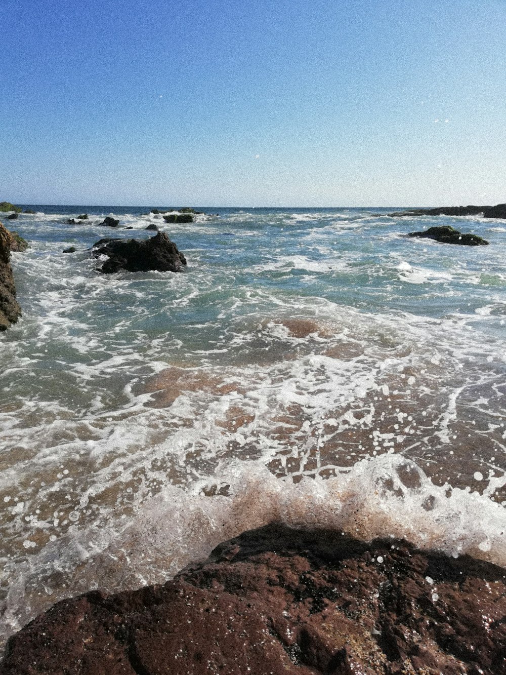 sea waves crashing on brown rock formation under blue sky during daytime