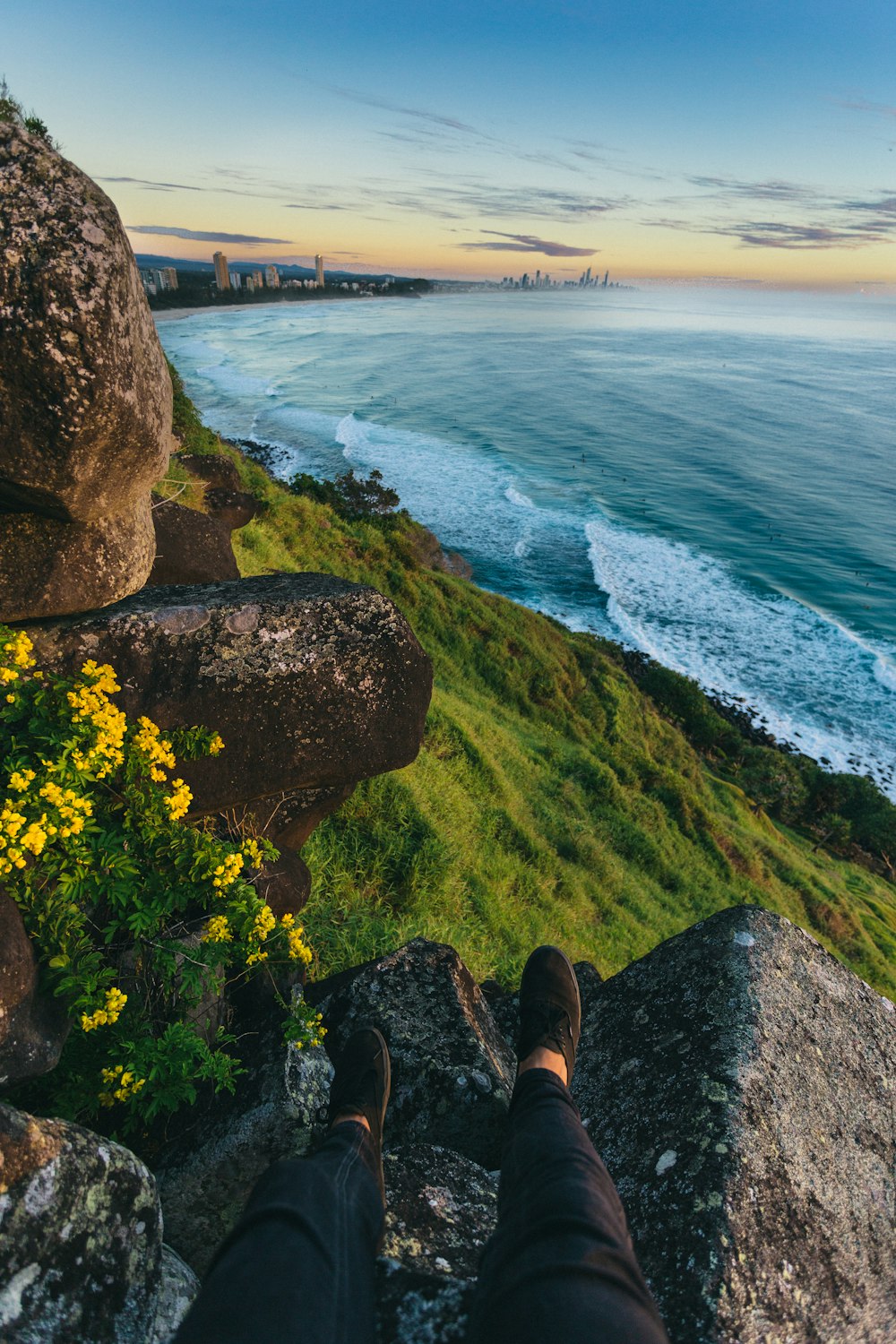 person in black pants and brown shoes sitting on rock near body of water during daytime