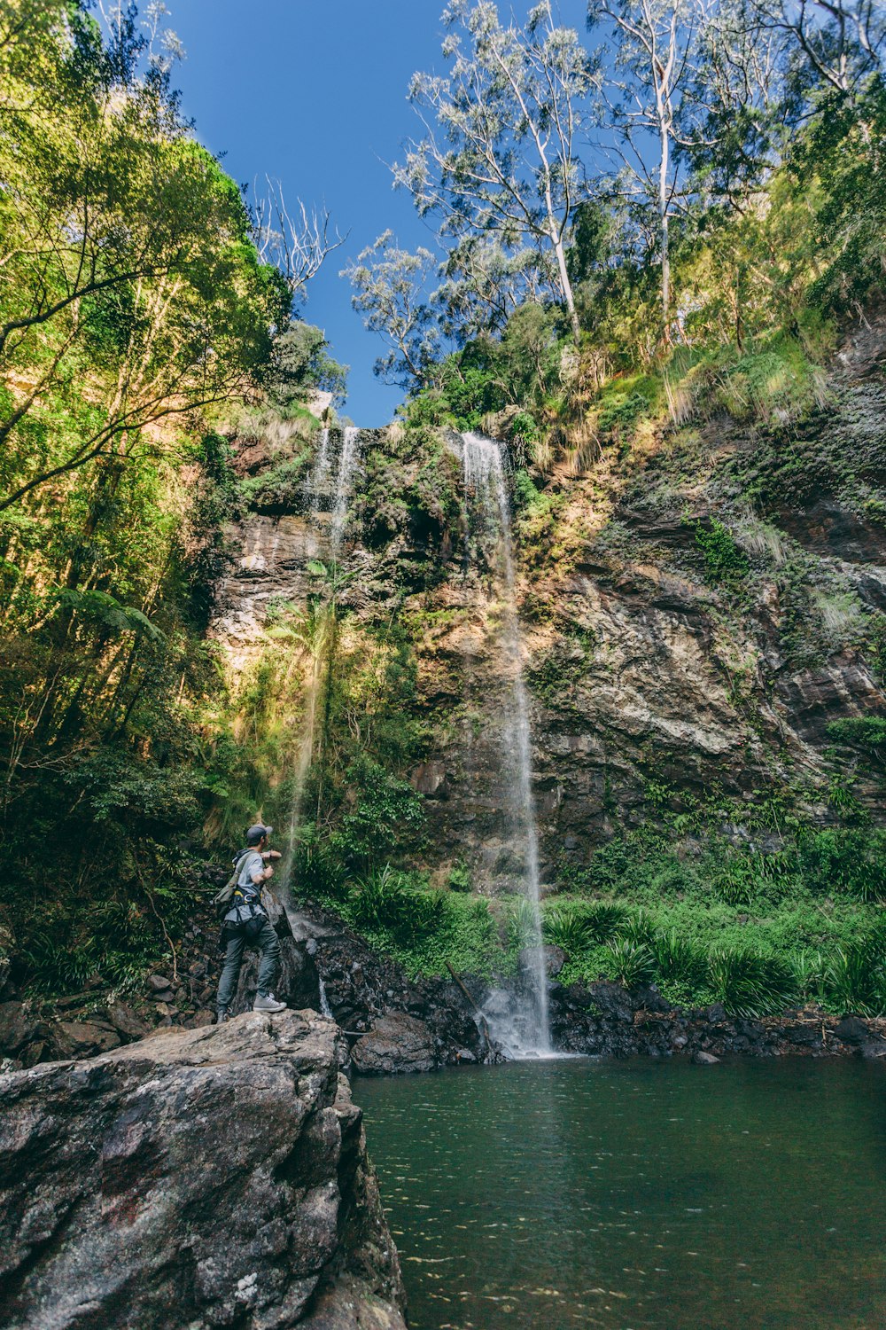 Mann in schwarzer Jacke sitzt tagsüber auf Felsen in der Nähe von Wasserfällen