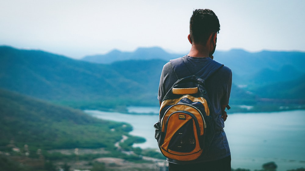 man in black shirt with brown backpack looking at mountains during daytime