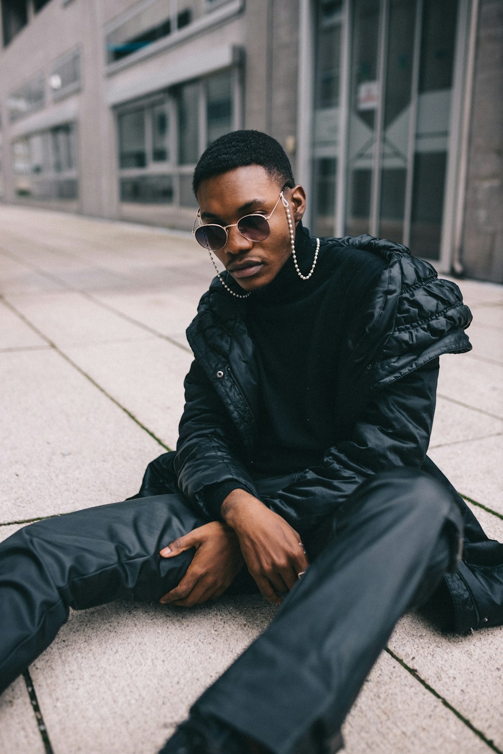 man in black leather jacket and black pants sitting on concrete floor during daytime