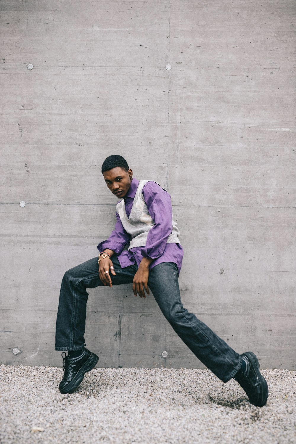 man in purple dress shirt and gray denim jeans sitting on concrete wall