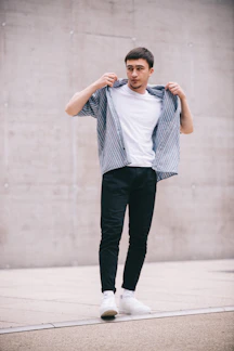 A stylish young man wearing a crisp white polo shirt and black denim jeans against a minimalist urban backdrop.