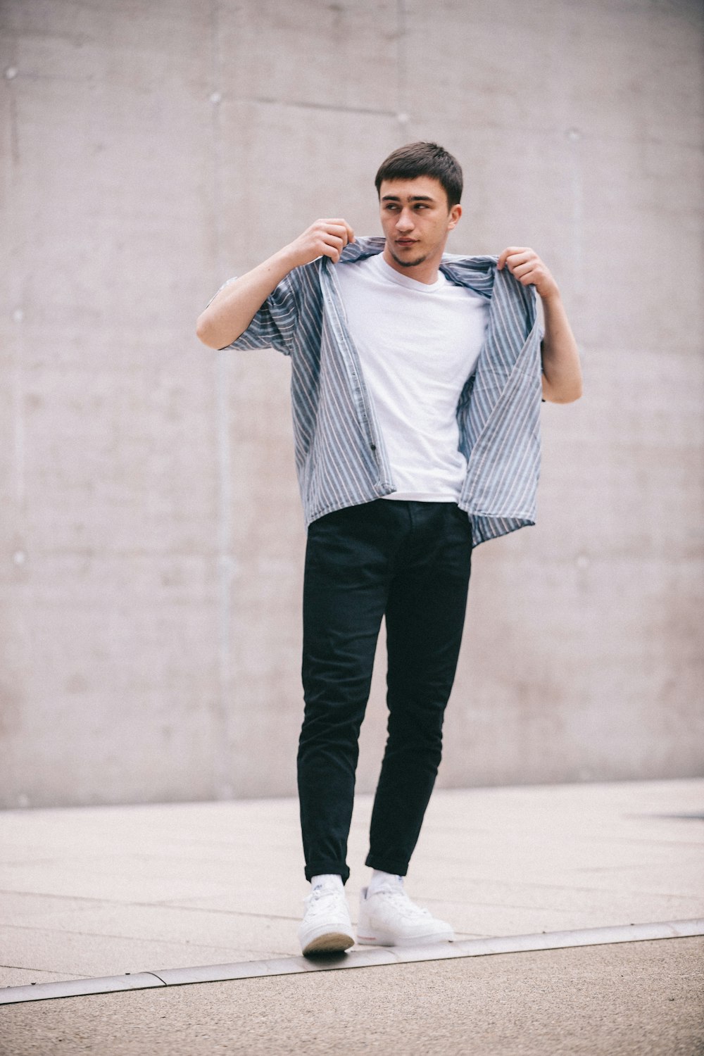 man in white and black striped dress shirt and black pants standing on gray concrete floor