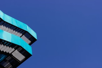 Angular, modern architectural structure with teal-colored panels is positioned against a deep blue, cloudless sky.