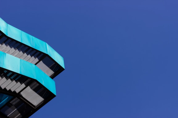 Angular, modern architectural structure with teal-colored panels is positioned against a deep blue, cloudless sky.
