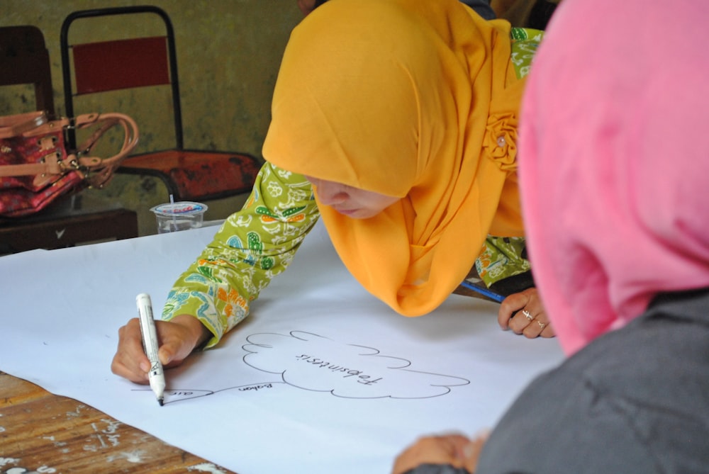 person in yellow hijab writing on white paper