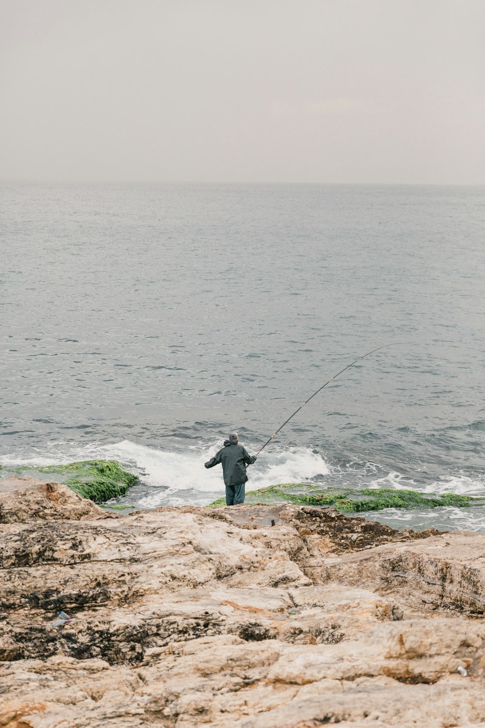 Mann in schwarzer Jacke beim Fischen auf See tagsüber