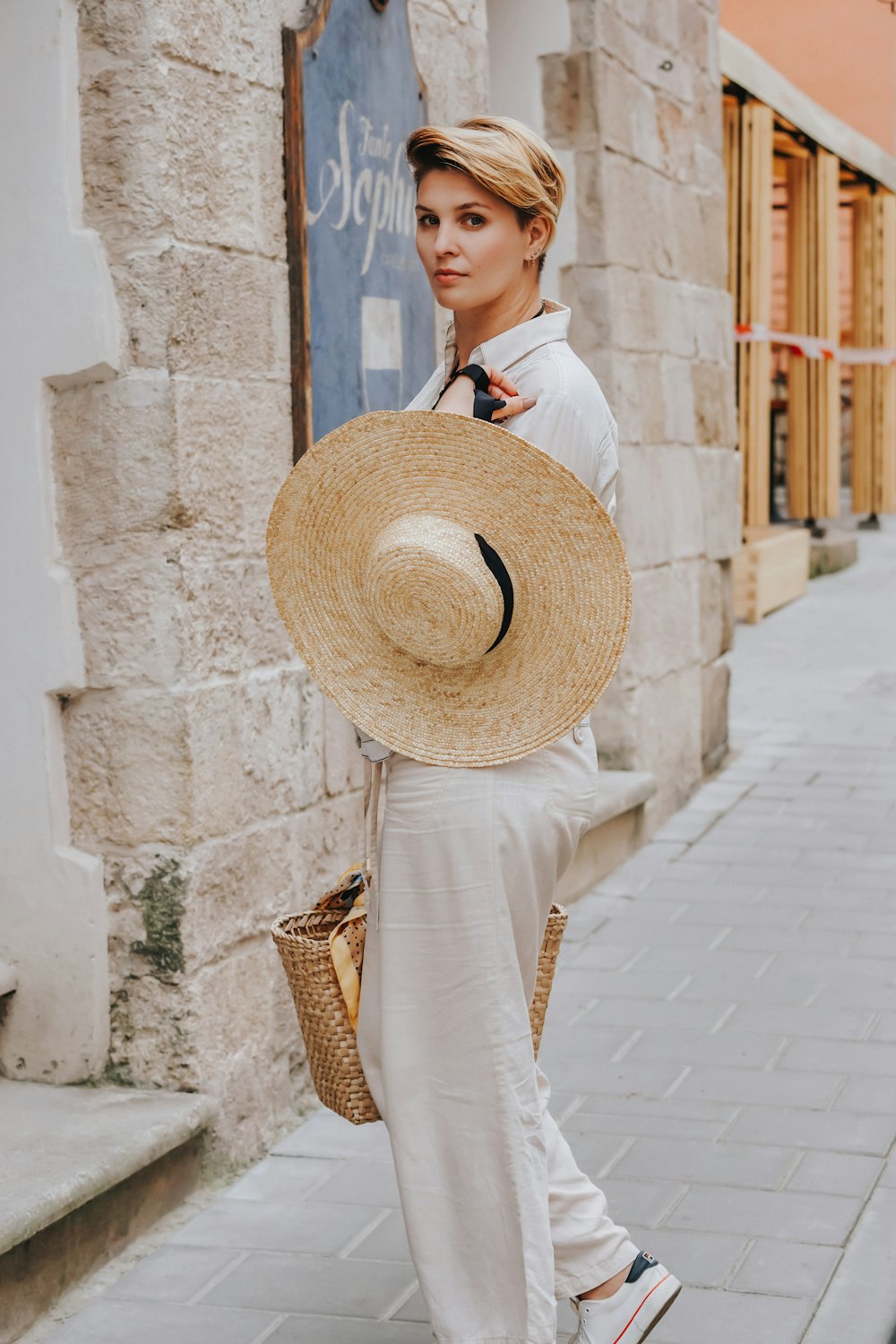 woman in white long sleeve shirt wearing brown straw hat standing beside concrete wall during daytime
