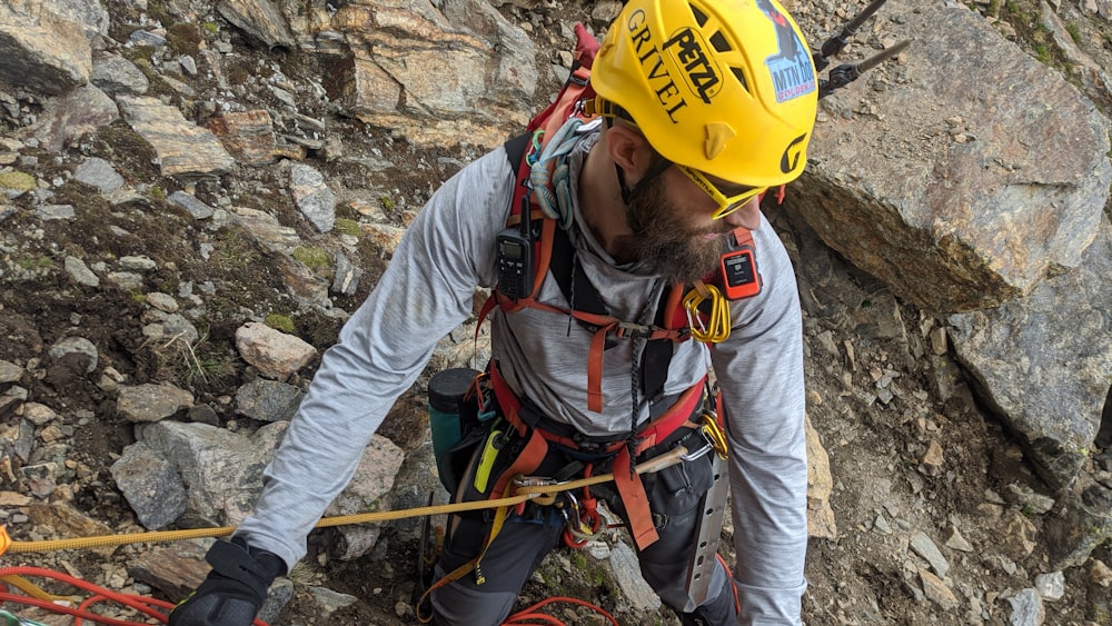 man in yellow hard hat and yellow helmet climbing on rocky mountain during daytime