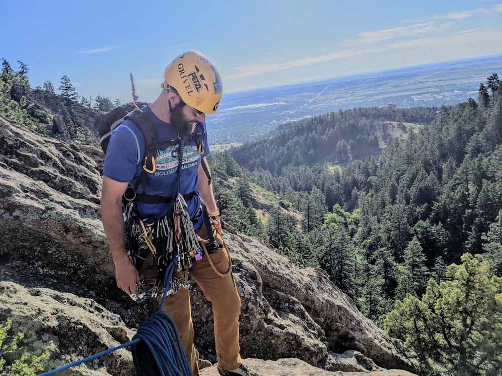 man in black t-shirt and blue pants with brown backpack standing on rocky mountain during