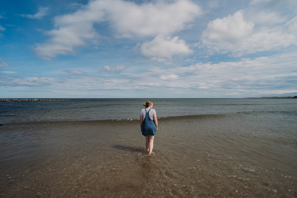 woman in blue denim jacket standing on brown sand under white clouds during daytime